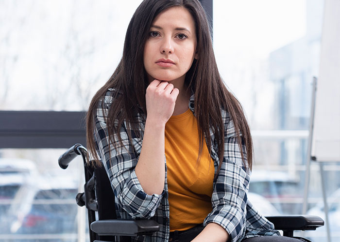 Young woman in a wheelchair wearing a plaid shirt and orange top, reflecting on unhinged things men said about looks in public
