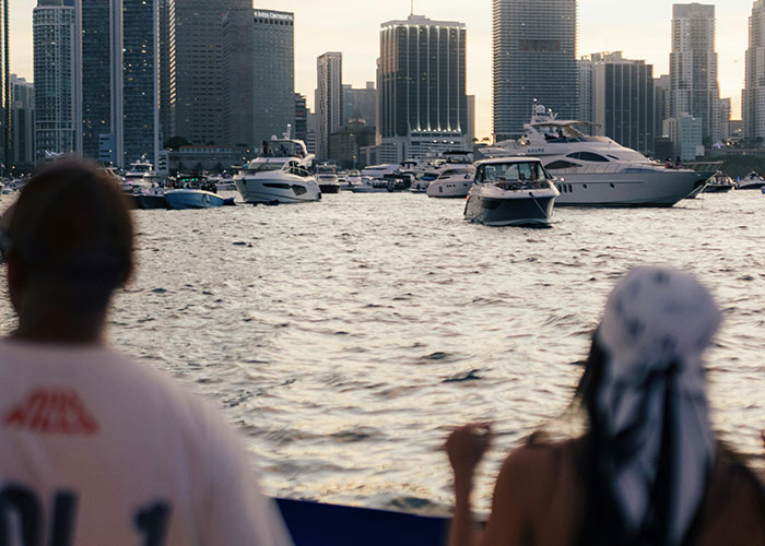 Two people watching boats on the water with city skyscrapers in the background during sunset.