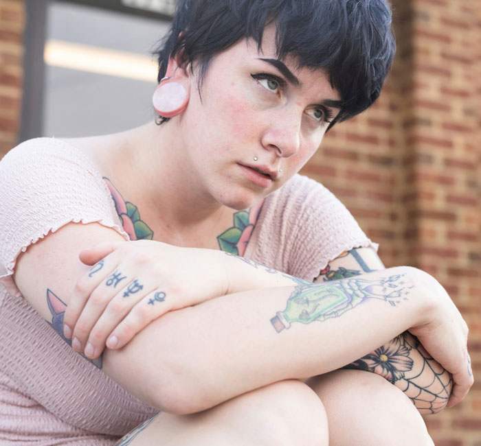 Young person with tattoos and piercings sitting outside looking thoughtfully concerned about toxic dating trends.