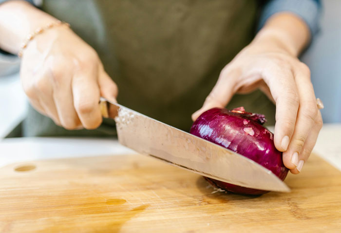 Hands chopping a red onion on a wooden cutting board illustrating old wives' tales about kitchen remedies and cooking tips.