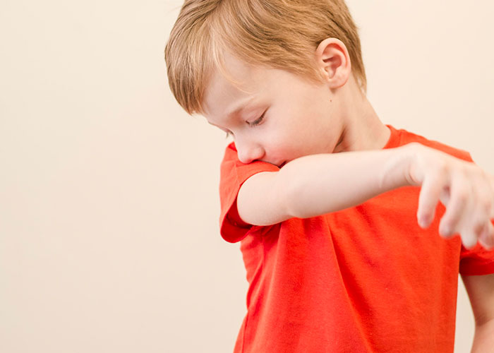 Young boy in an orange shirt sneezing into his arm, illustrating wildest encounters buffet workers might face.