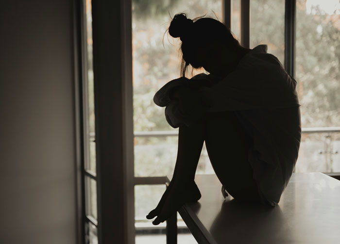 Silhouette of a millennial sitting alone by a window, reflecting on the biggest lies they were told growing up.