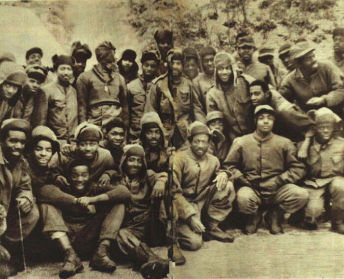 Group of African American soldiers in vintage military uniforms posed outdoors, representing African American military history.