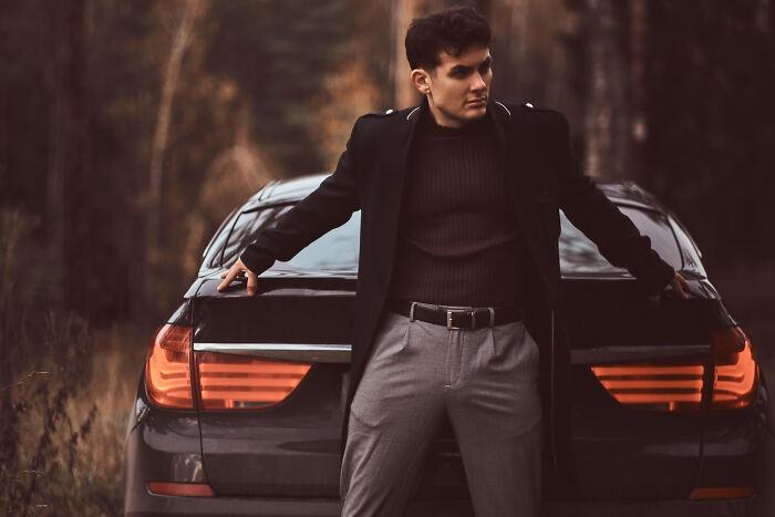 Young man leaning on a car looking away, illustrating behaviors that may indicate someone is insecure in a moody outdoor setting.