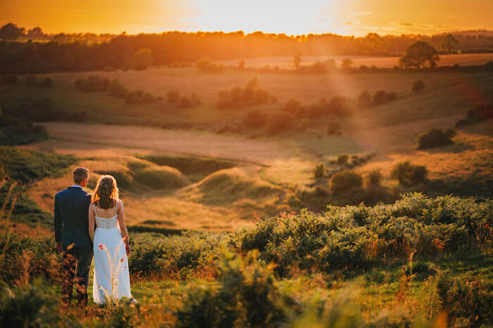Bride and groom walking through scenic countryside at sunset, captured in unforgettable wedding photos for inspiration.