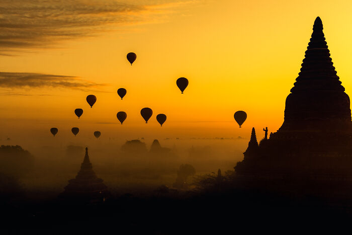 Silhouettes of hot air balloons floating over ancient temples at sunrise in a breathtaking travel photo.