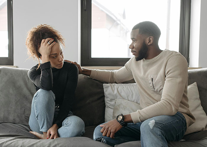 Couple on sofa discussing postpartum help and concerns about balancing grandparent involvement after baby arrives. Couple on sofa discussing postpartum help and concerns about balancing grandparent involvement after baby arrives.