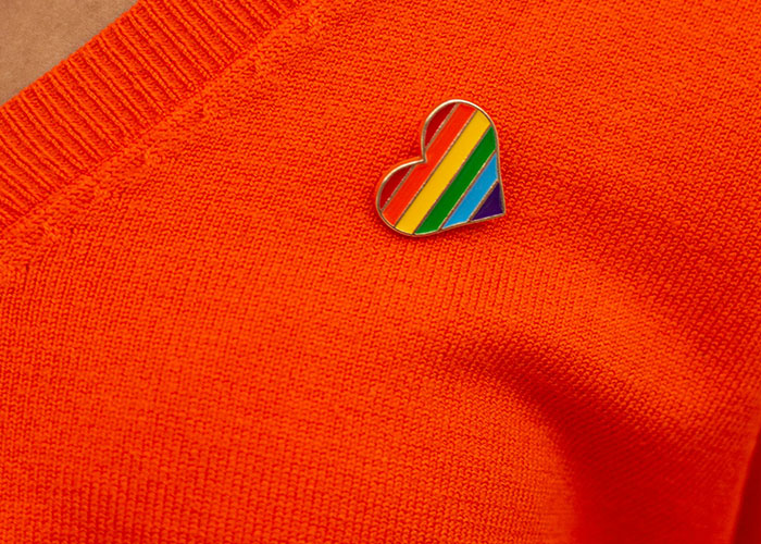Heart-shaped rainbow pin on an orange sweater, symbolizing bluntness and emotions around travel with a friend conflict. Heart-shaped rainbow pin on an orange sweater, symbolizing bluntness and emotions around travel with a friend conflict.