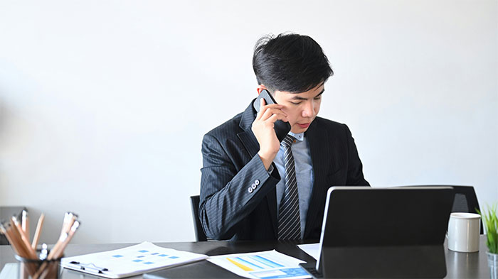 Businessman in a suit talking on phone, reviewing documents at desk, depicting insurance company denies employee claim scenario. Businessman in a suit talking on phone, reviewing documents at desk, depicting insurance company denies employee claim scenario.
