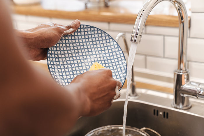 Man washing a patterned plate by the sink with running water demonstrating a shower trick lesson.