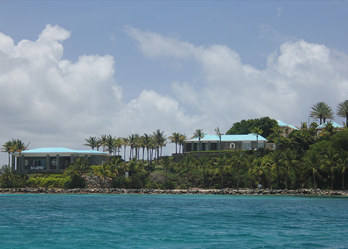 Coastal view of tropical island houses surrounded by palm trees under a cloudy blue sky, evoking creepy facts vibe.