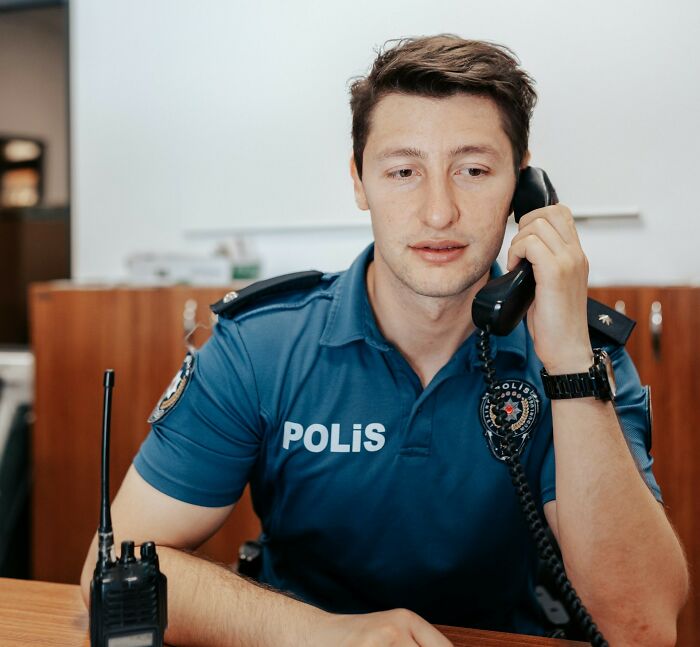 Police officer in uniform talking on a desk phone with a walkie-talkie, showing the challenges police face daily.