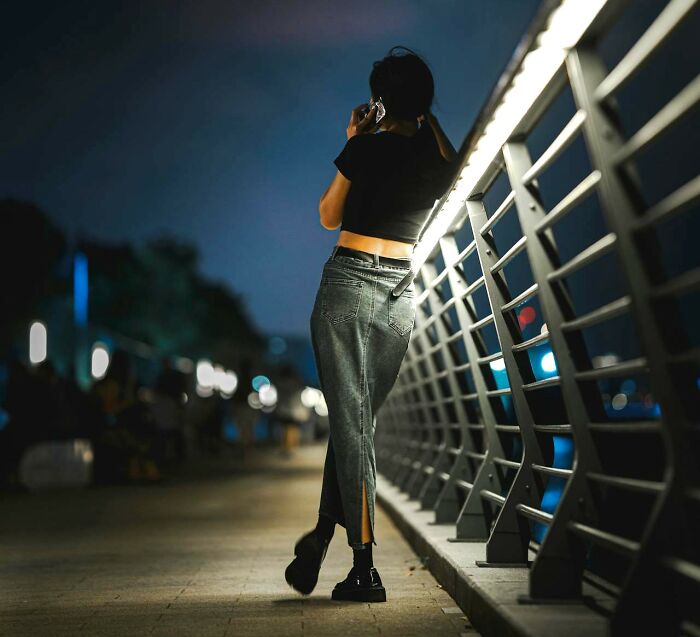 Young woman standing on a bridge at night, talking on the phone, illustrating unresolved personal mysteries people face.