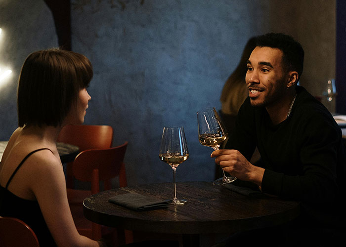 Couple on an awkward date in a dimly lit restaurant, holding wine glasses and struggling to connect during the conversation.