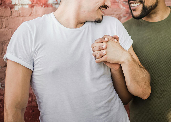 Two men smiling and holding hands showing affection, highlighting engagement and relationship trust issues.