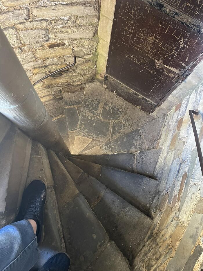 Narrow stone death stairs in an old building with worn steps and a rusty door at the bottom of the spiral.