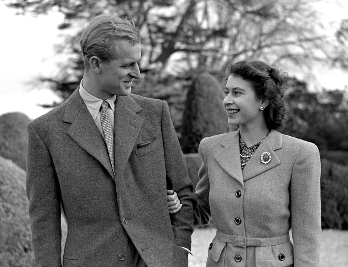 Black and white photo of two good looking famous names from history smiling and walking outdoors in vintage attire.