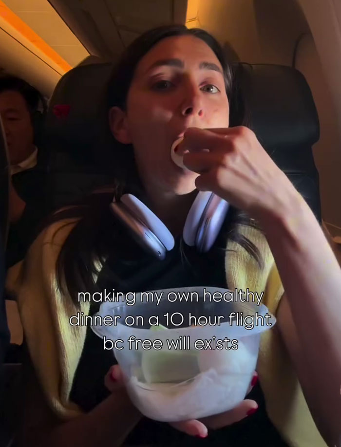 Plane passenger eating salad mid-flight with headphones around neck, making her own healthy dinner on a long flight. Plane passenger eating salad mid-flight with headphones around neck, making her own healthy dinner on a long flight.