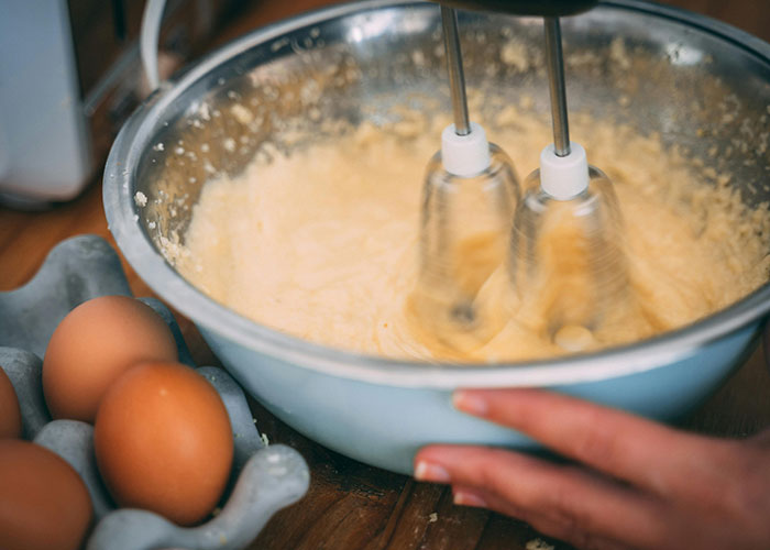 Close-up of a hand mixing batter with an electric mixer beside fresh eggs, related to buffet workers’ wildest encounters.