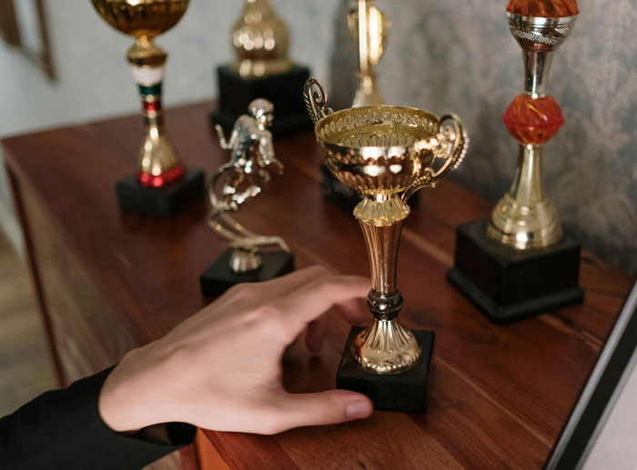 Hand reaching to grab a gold trophy among several awards, symbolizing achievement and biggest lies millennials were told growing up