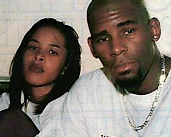 Rapper R Kelly wearing a white shirt and chain, seated next to a woman, both looking directly at the camera. Rapper R Kelly wearing a white shirt and chain, seated next to a woman, both looking directly at the camera.