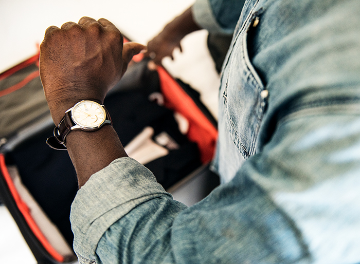Man checking wristwatch while packing suitcase, focusing on sticking to his schedule and being on time.