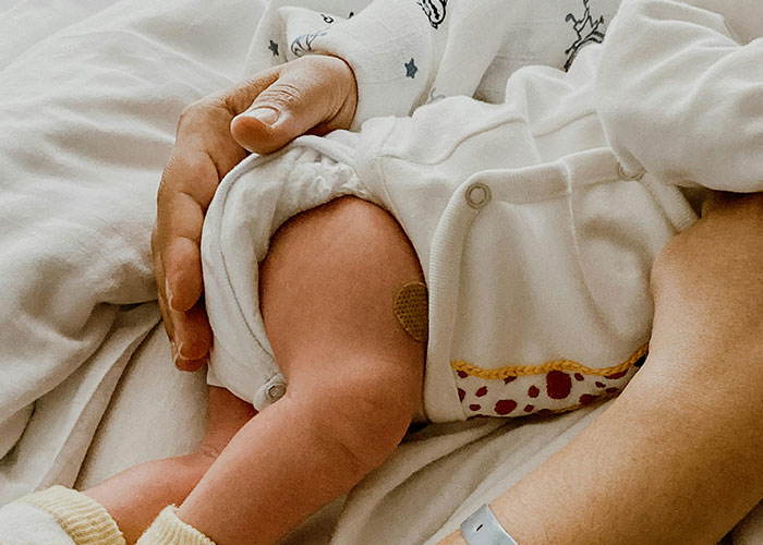 Father’s hand gently holding newborn baby resting on a white blanket, capturing a birthing room moment for the first time.