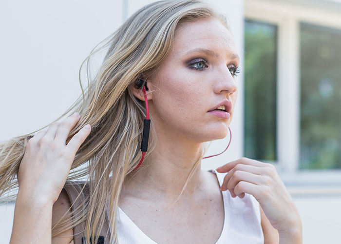 Young woman with earbuds adjusting her hair outdoors, reflecting on unhinged things men have said about her looks in public.
