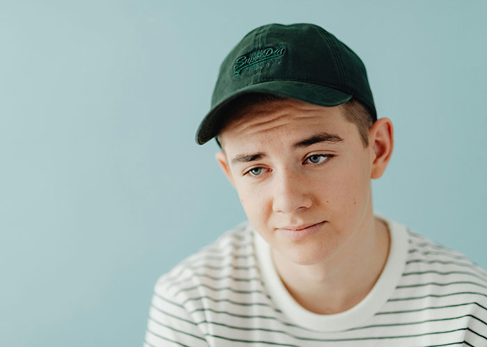 Young man wearing a black cap and striped shirt, looking thoughtful in a casual indoor setting, showing take one for the team moment.