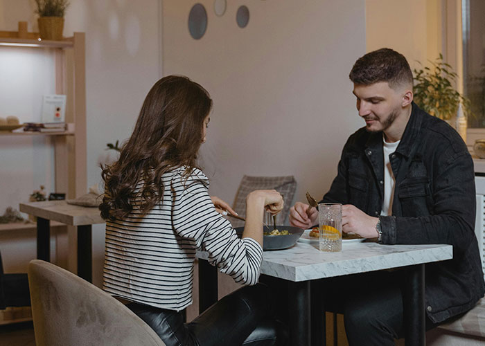 Young couple having an awkward dinner date at a small restaurant, appearing uncomfortable and avoiding eye contact.