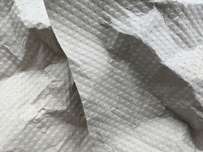 Crinkled textured paper close-up showing details of folds and shadows in a neutral gray tone background.