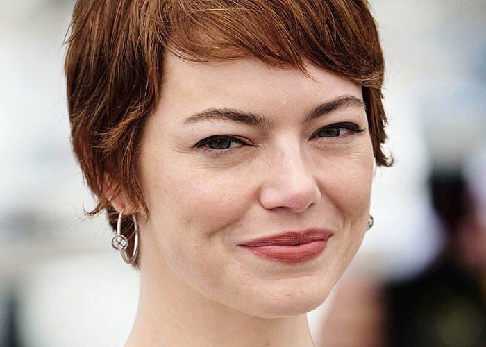 Close-up of a smiling woman with short red hair and earrings, illustrating what celebrities were doing before fame found them.