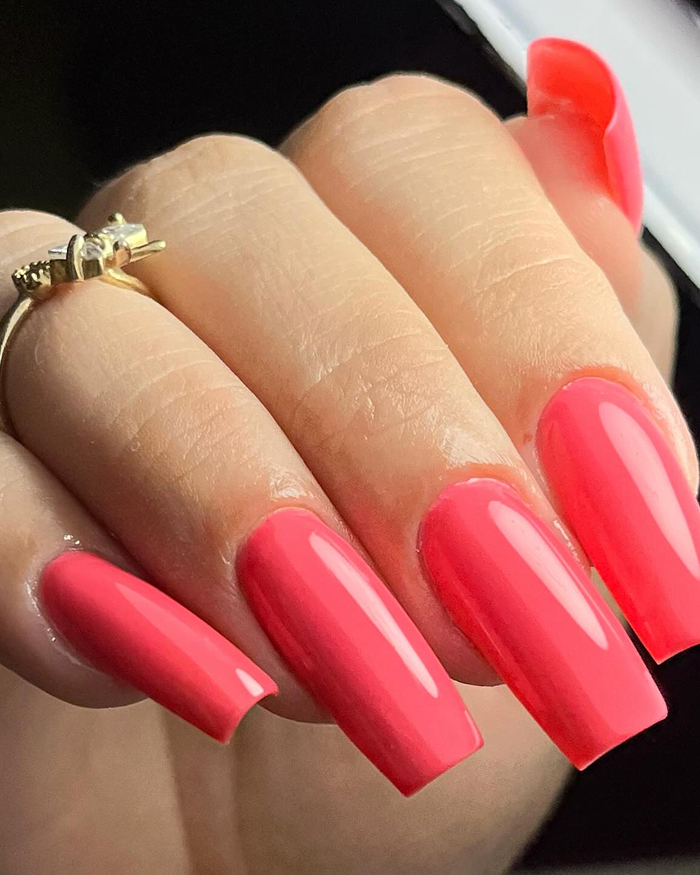 Glossy long nails with orange and pink gradient tips on brown skin showcasing summer nails trends.