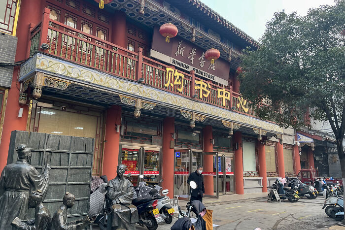 Exterior of a grandiose and cosy bookstore with traditional architectural details and statues in front, showcasing magical ambiance