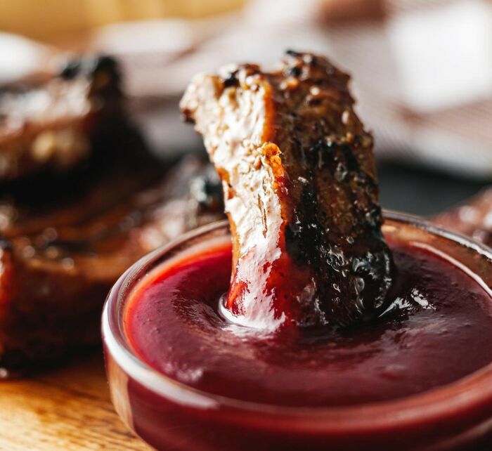 Grilled meat being dipped into barbecue sauce, illustrating Americans reveal things non-Americans do like breaking spaghetti.