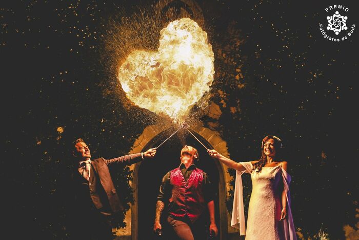 Couple and performer creating a heart-shaped fire display at night in an unforgettable wedding photo.