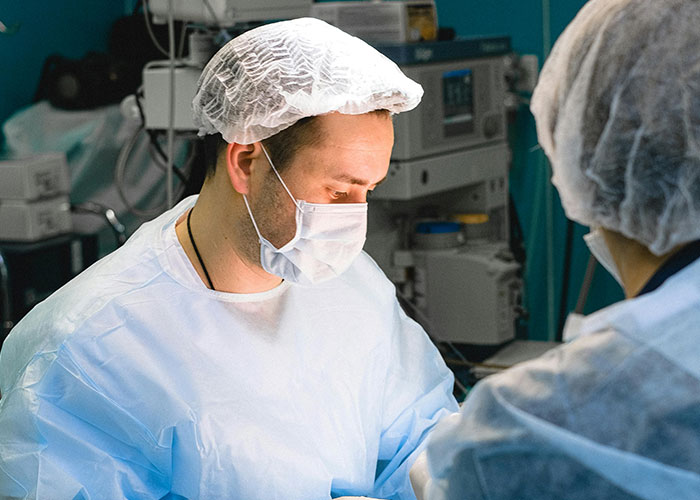 Man wearing surgical scrubs and mask inside a hospital birthing room, experiencing the moment as a new dad.