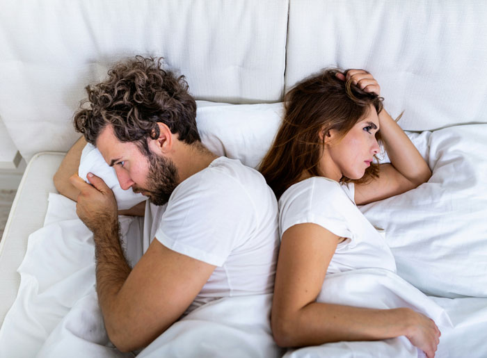 Couple in bed facing away from each other looking upset, illustrating toxic dating trends in modern relationships.