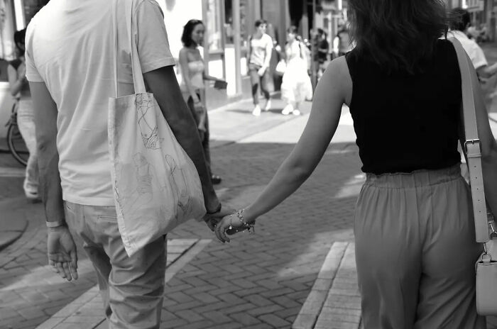 Black and white street shot of a couple holding hands, capturing the poetry of everyday life in an urban setting.