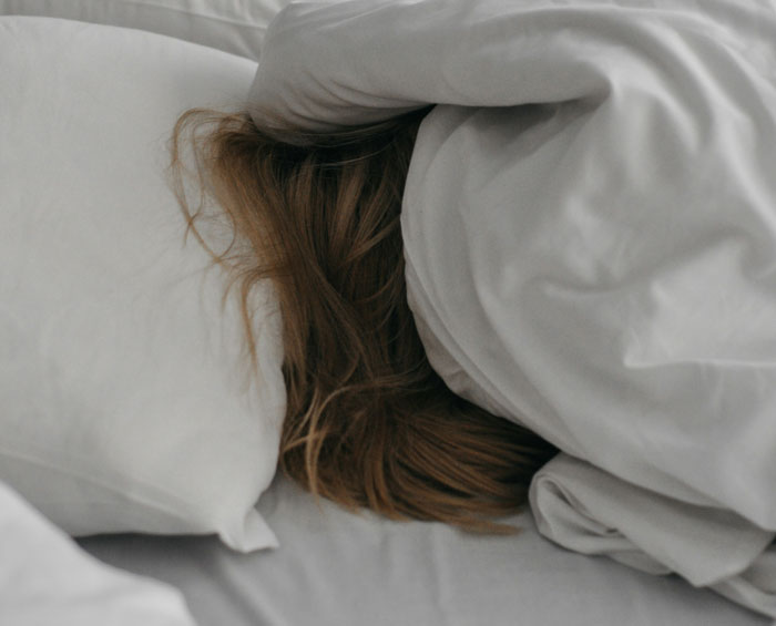 Person hiding under white blankets in bed, illustrating regret and reflection on biggest life mistakes.