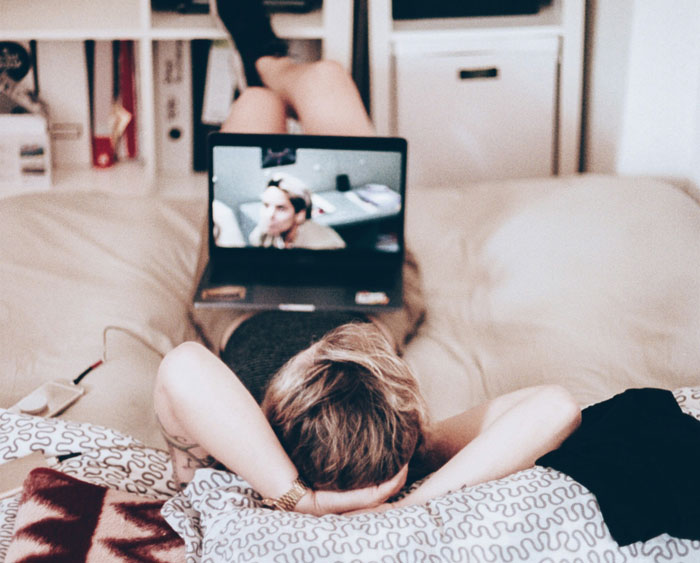 Millennial lounging on couch watching movie on laptop, reflecting on biggest lies they were told growing up.