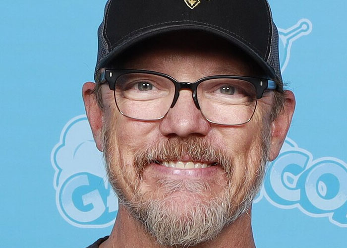 Middle-aged man with glasses and a cap smiling, related to celebrities before fame stories.