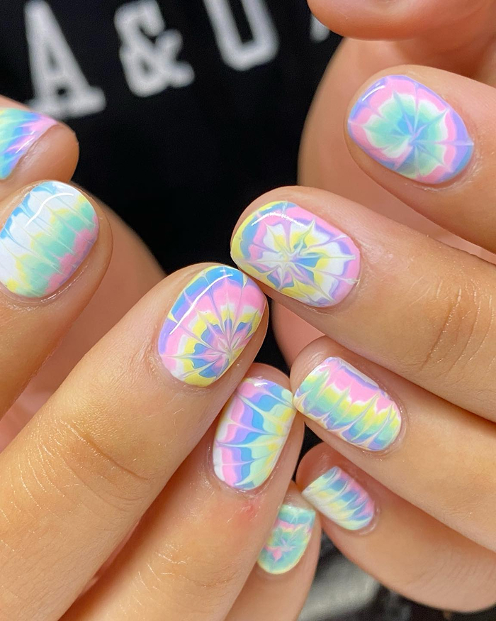 Pastel tie-dye summer nails in soft pink, blue, yellow, and green shades on short, rounded nails.