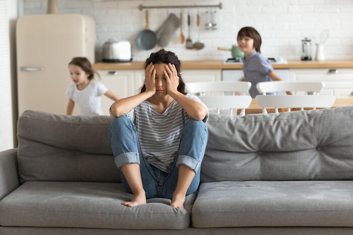 Woman frustrated on couch while two children play in background, illustrating moments people committed to a lie way too hard.
