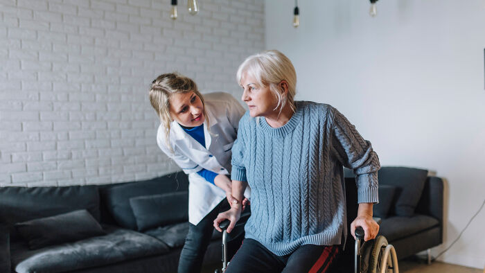 A healthcare professional assisting an elderly woman using a walker in a cozy living room setting. - 17