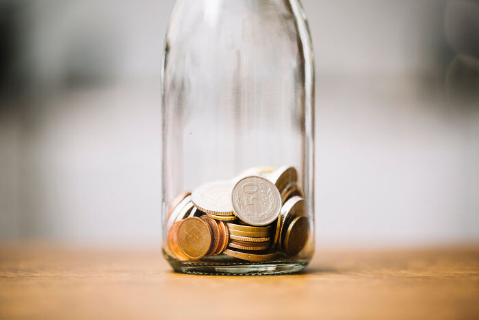 Glass jar partially filled with coins representing poor people habits related to money and savings.