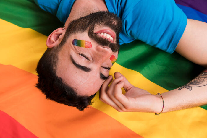 Man with rainbow face paint smiling while lying on a colorful rainbow flag, representing secrets parents kept from their kids.