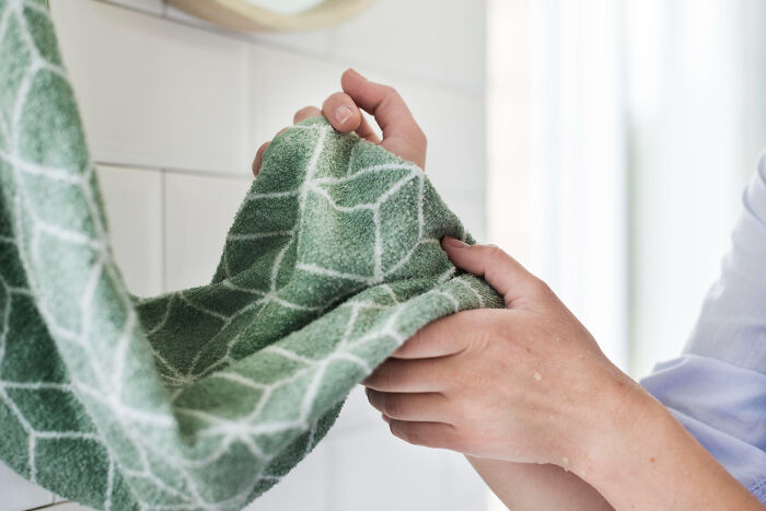 Hands drying nails with a green patterned towel, illustrating a common nail care habit related to biting nails.