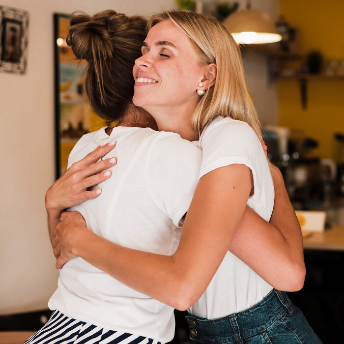 Two women in casual clothes sharing a warm hug, symbolizing emotional support and healing from childhood struggles.