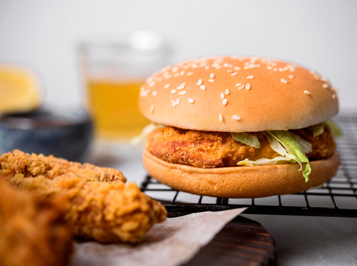Crispy fried chicken sandwich with lettuce and golden fried chicken pieces on a cooling rack and wooden board.